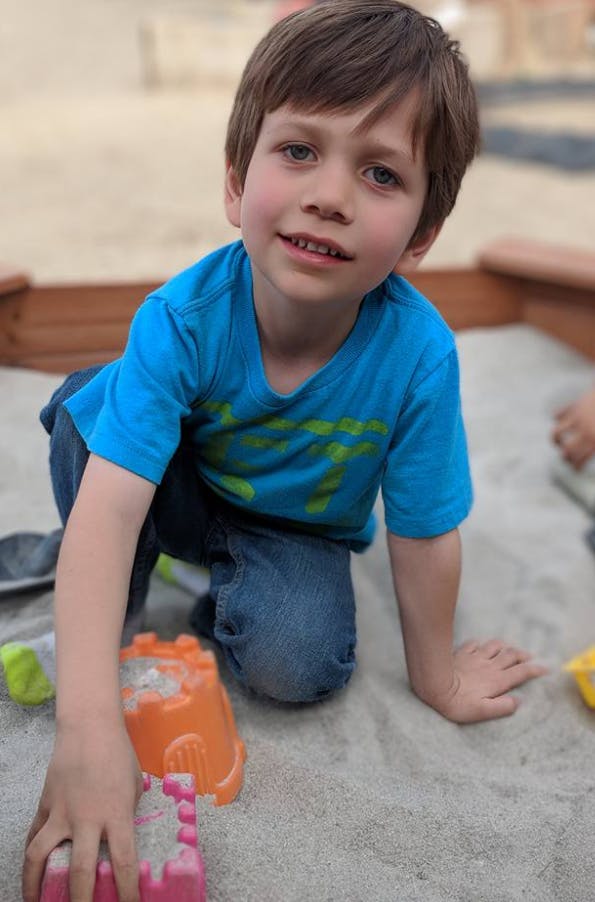 Child kneeling in a sandbox with sand toys