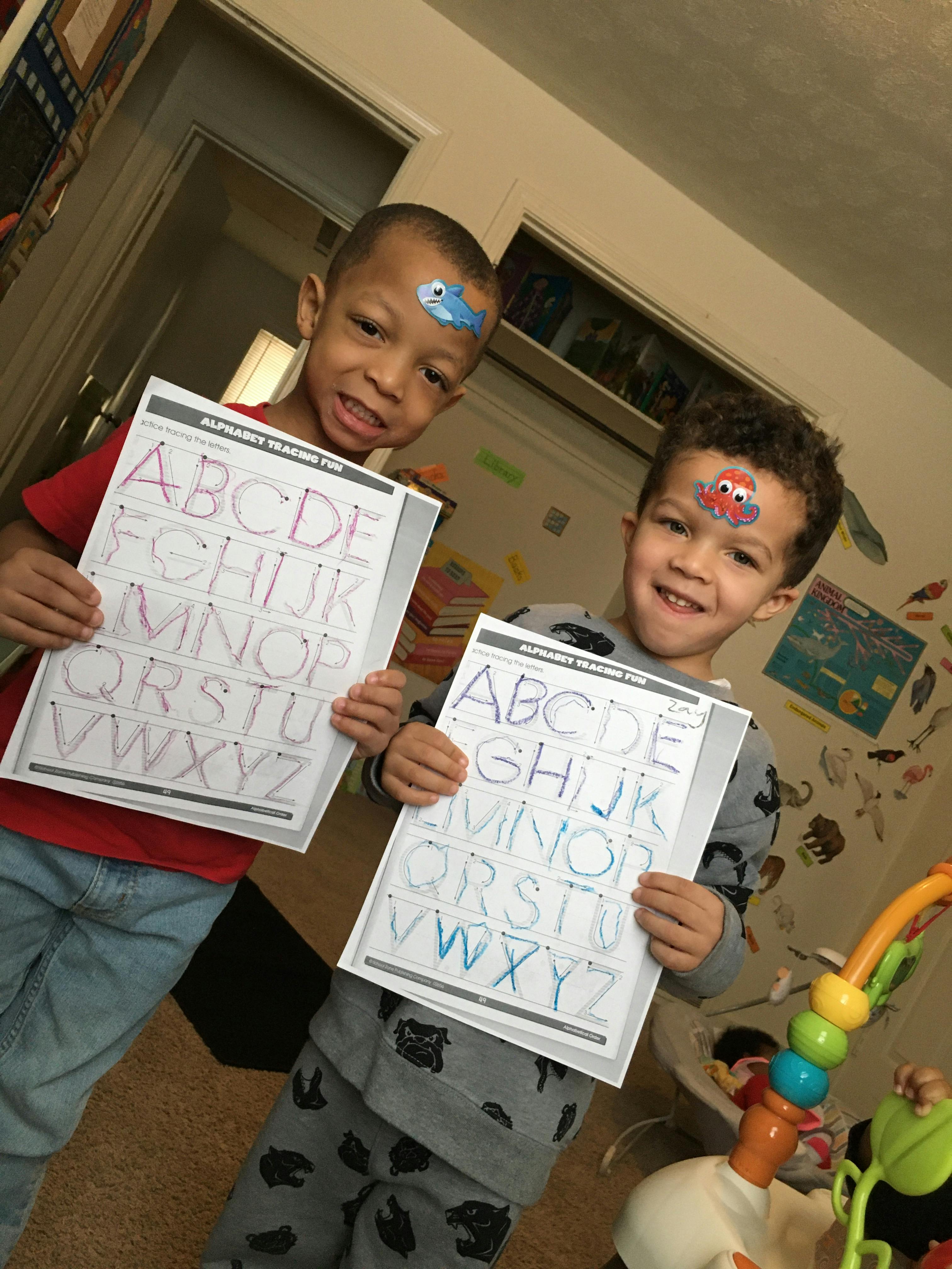 Two children holding up alphabet tracing sheets