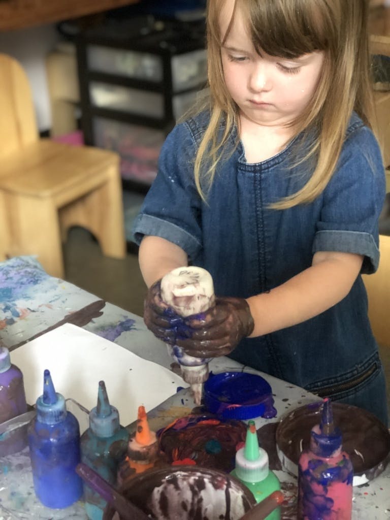 Child squeezing paint from a bottle, hands covered in paint