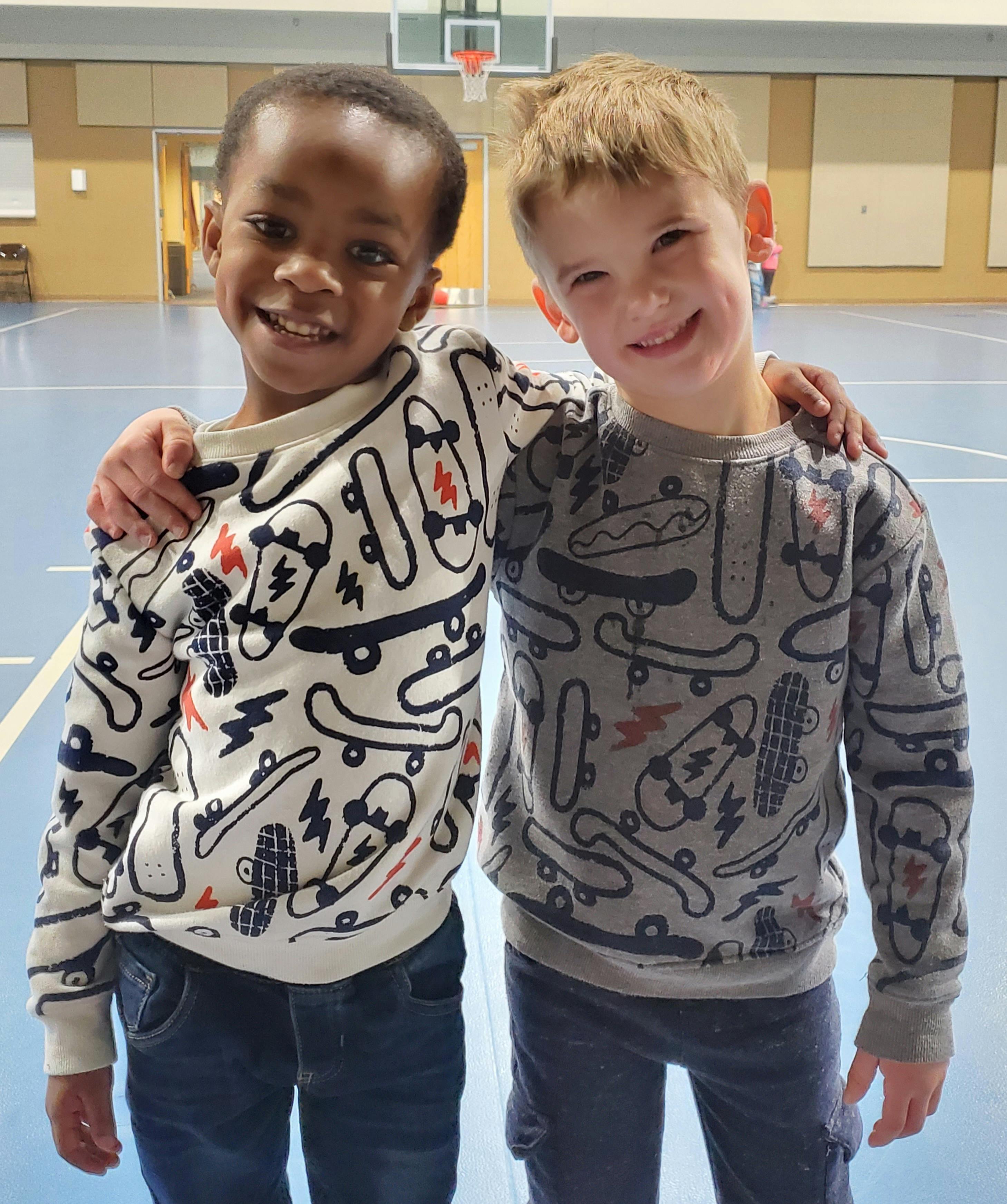 Two children standing with arms around each other in a gym