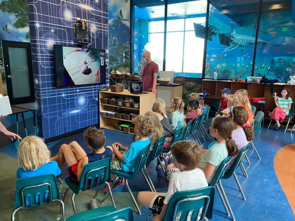Adult speaking to a group of children watching a screen in a classroom