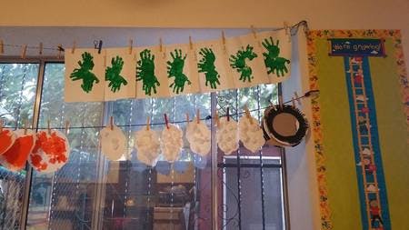 Children's artwork with green handprints and white cutouts hanging on a string