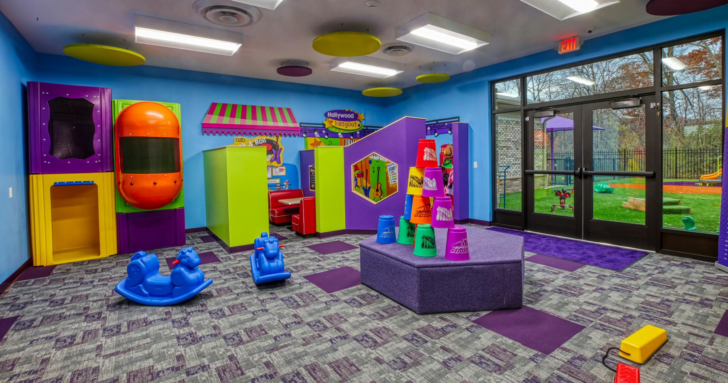 Colorful indoor play area with rock horses, cubbies, and large window to outdoor playground