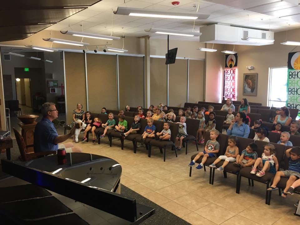 Person speaking to a group of children and adults in a room