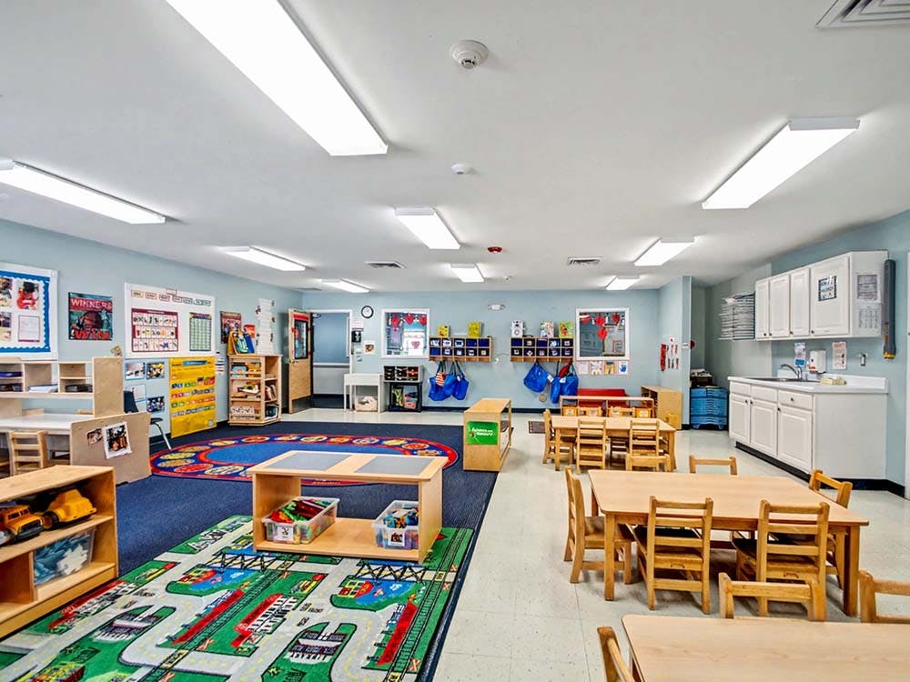 Empty children's classroom with small tables and a play rug