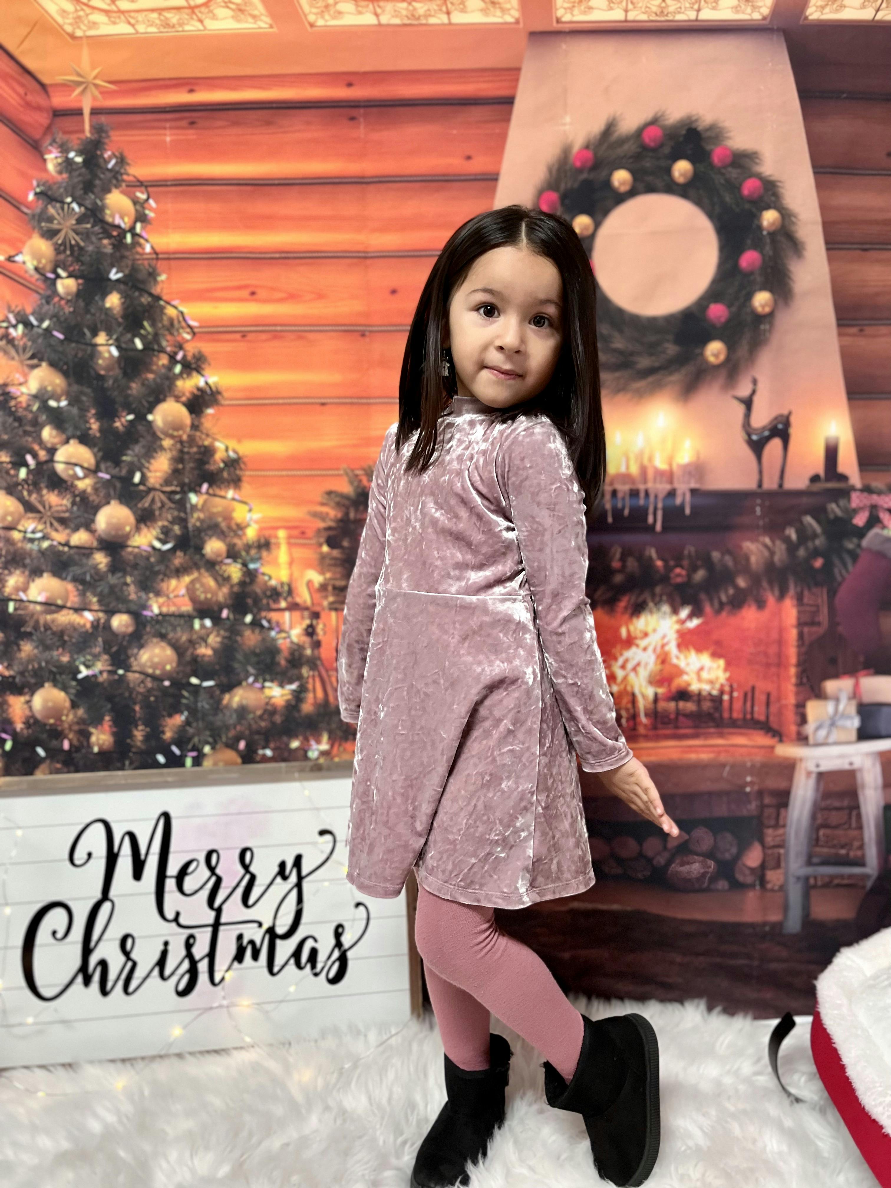 Child standing in front of a Christmas tree and fireplace with a sign that says "Merry Christmas"