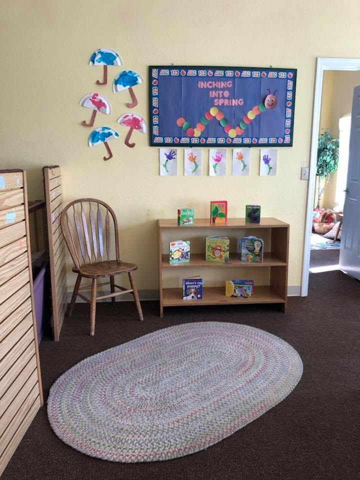 Classroom with bulletin board, bookshelf, chair, and oval rug