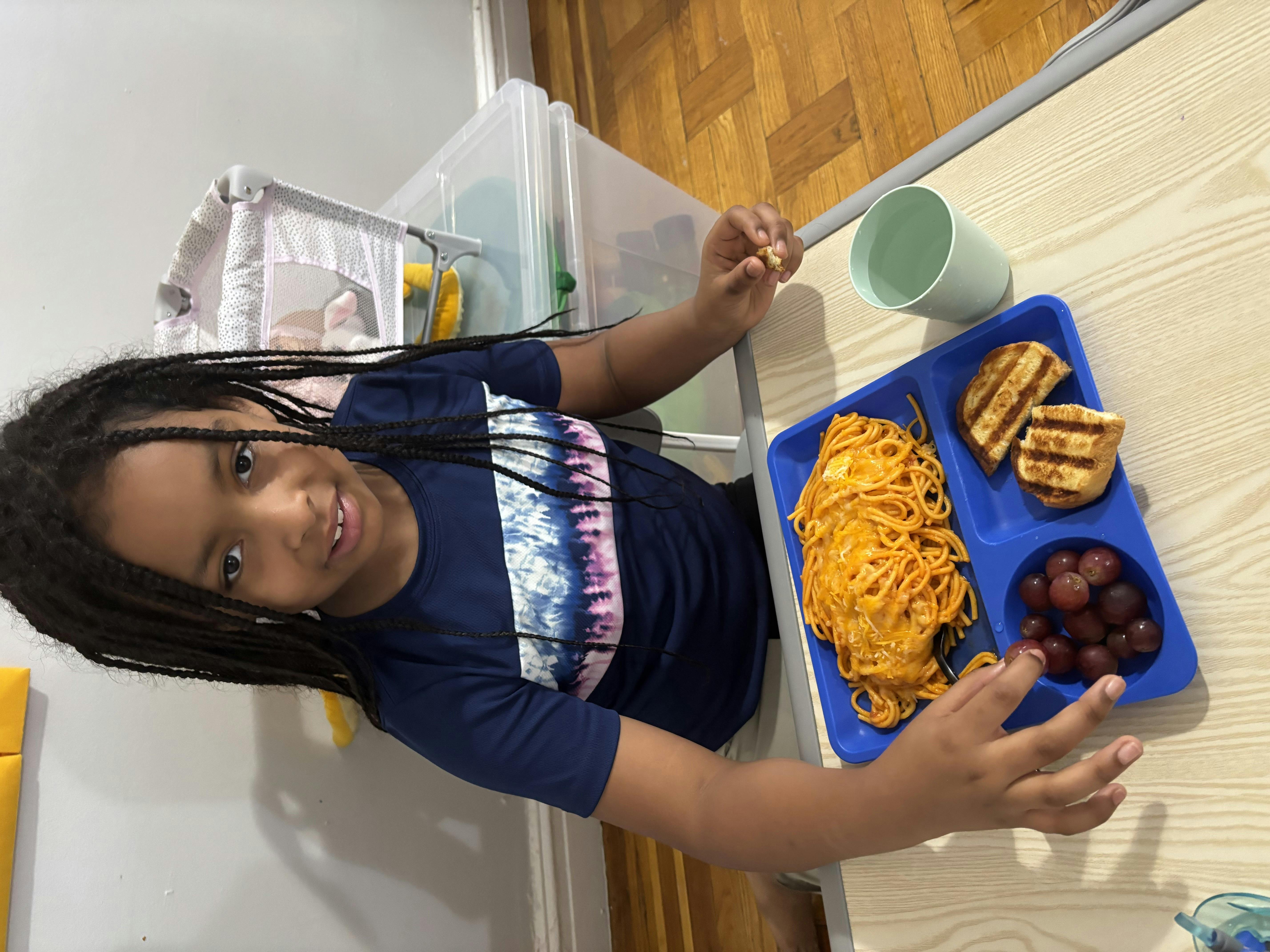 Child sitting at a table with a plate of spaghetti, toast, and grapes
