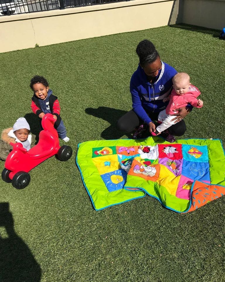 Person holding a baby, two children playing with a ride-on toy and blanket