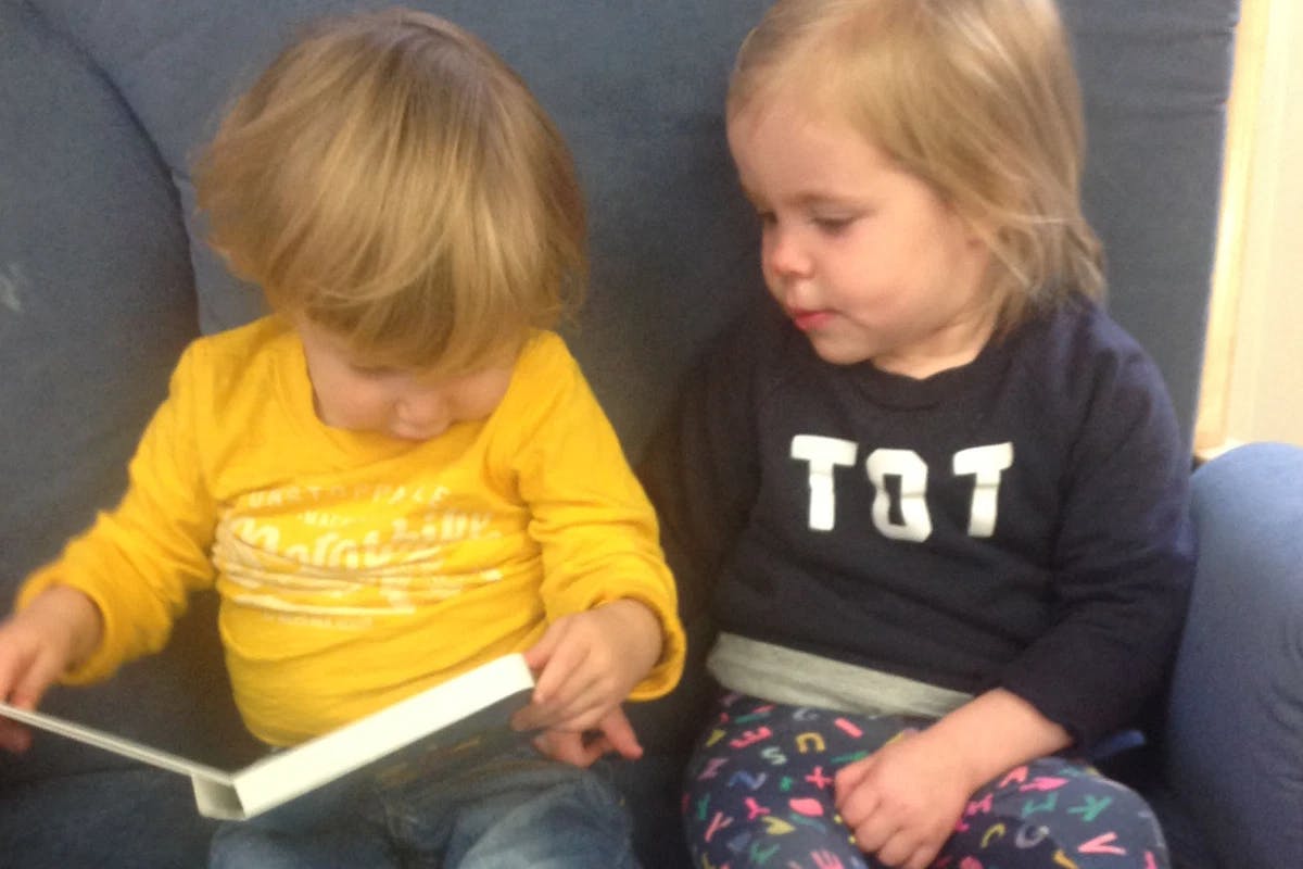 Two children sitting together, one looking at a book