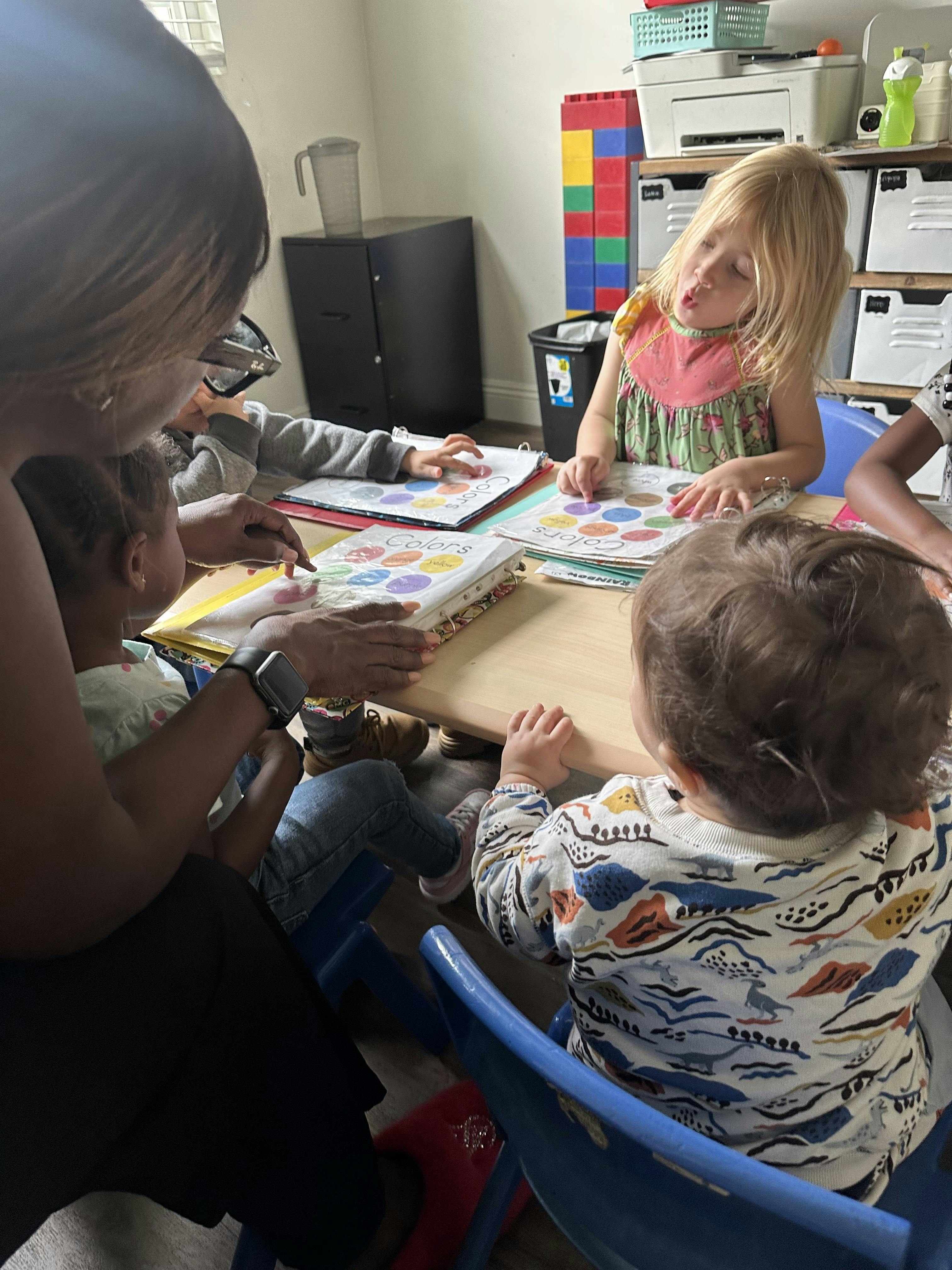 Adult assisting children with a color learning activity at a table