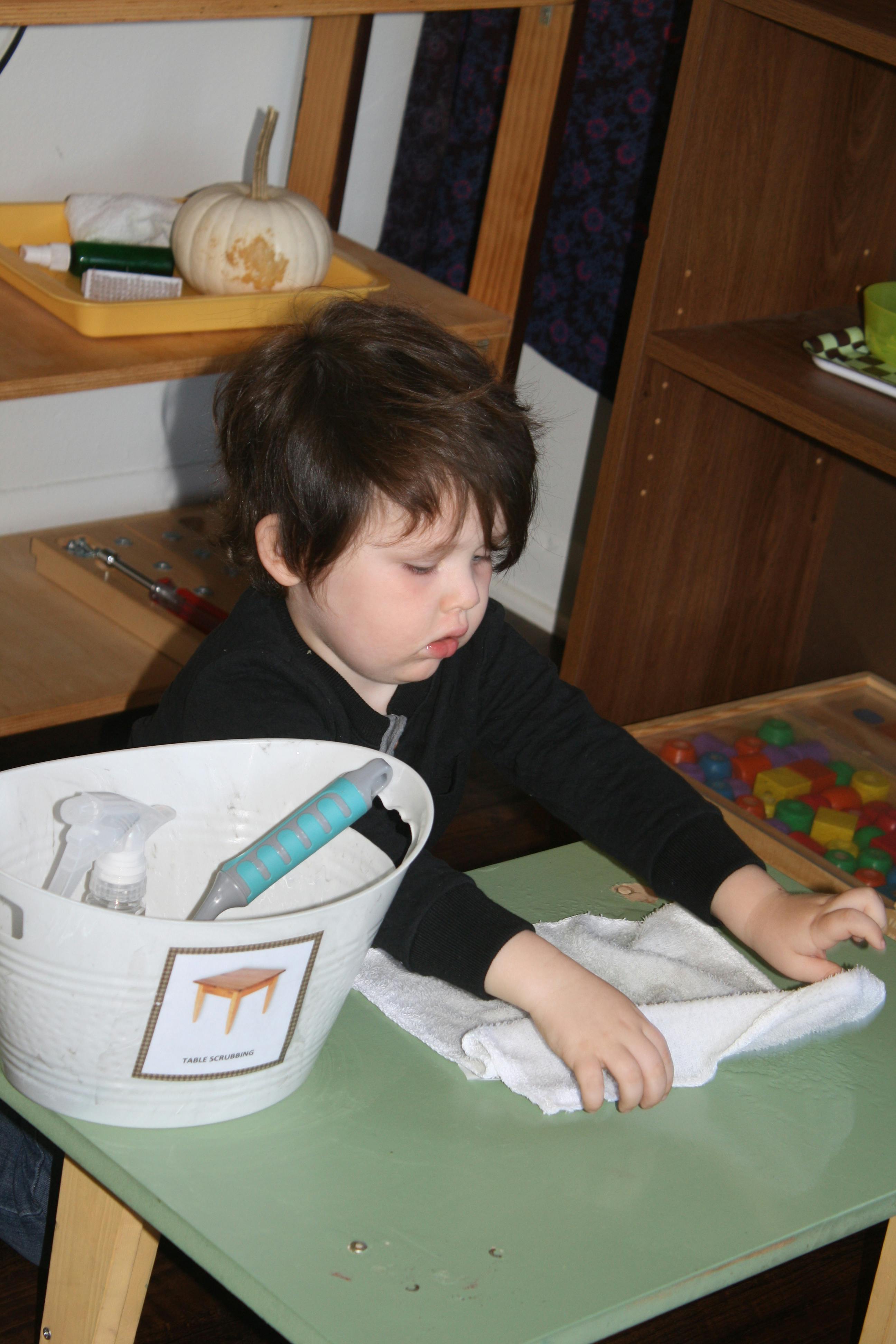 Child folding a white cloth on a green table