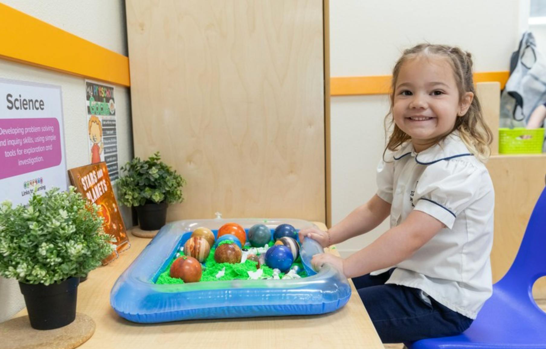 Child smiling while playing with a sensory bin containing planets
