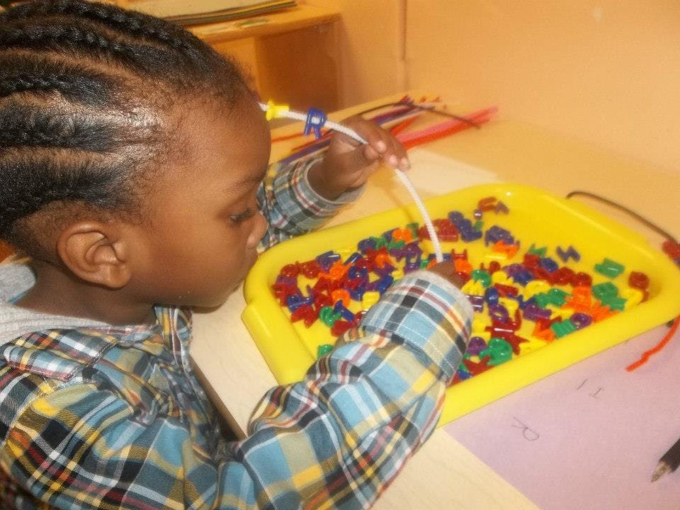 Child playing with colorful beads in a yellow tray