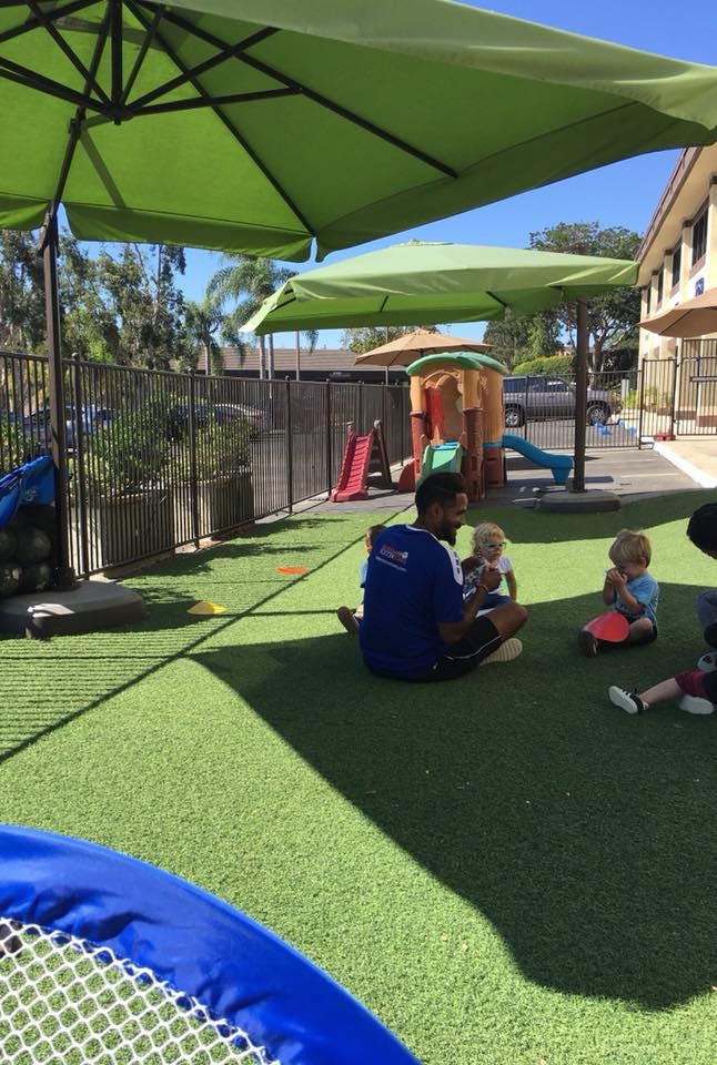 Adult and two children sitting on artificial grass under umbrellas