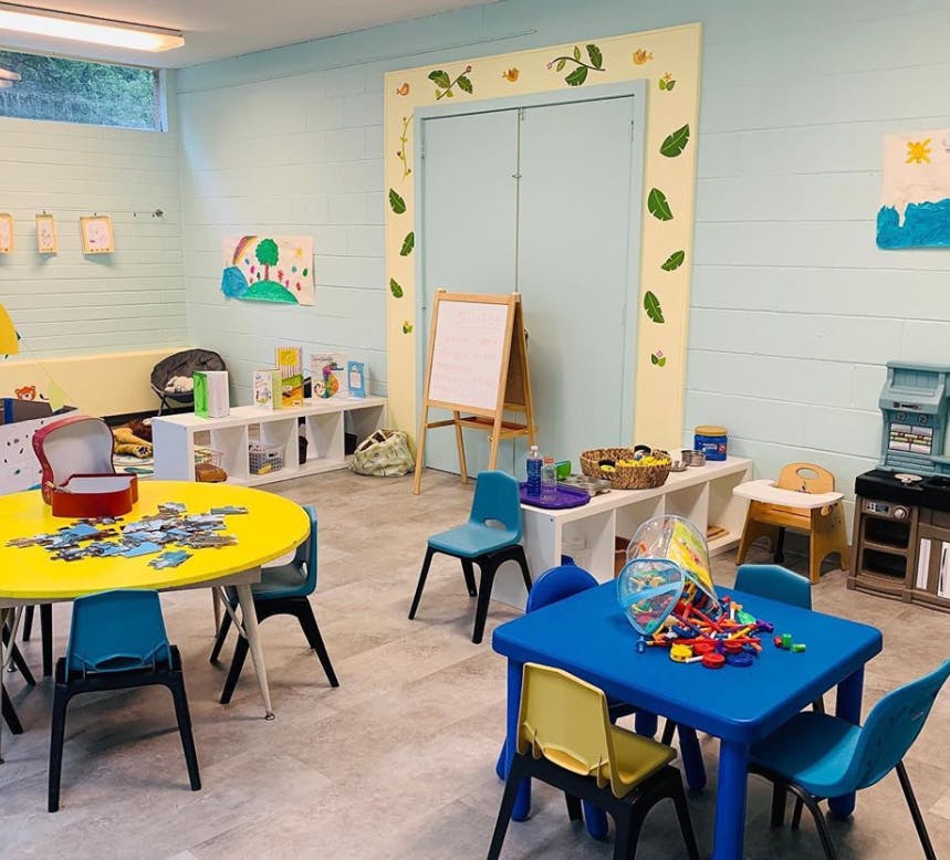 Classroom with small tables and chairs, an easel, and shelves with toys and art supplies