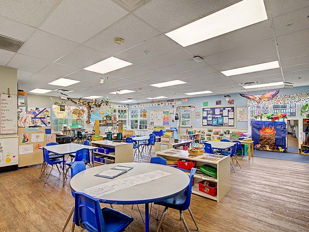 Classroom with small tables and chairs, decorated walls and ceiling, wood floor