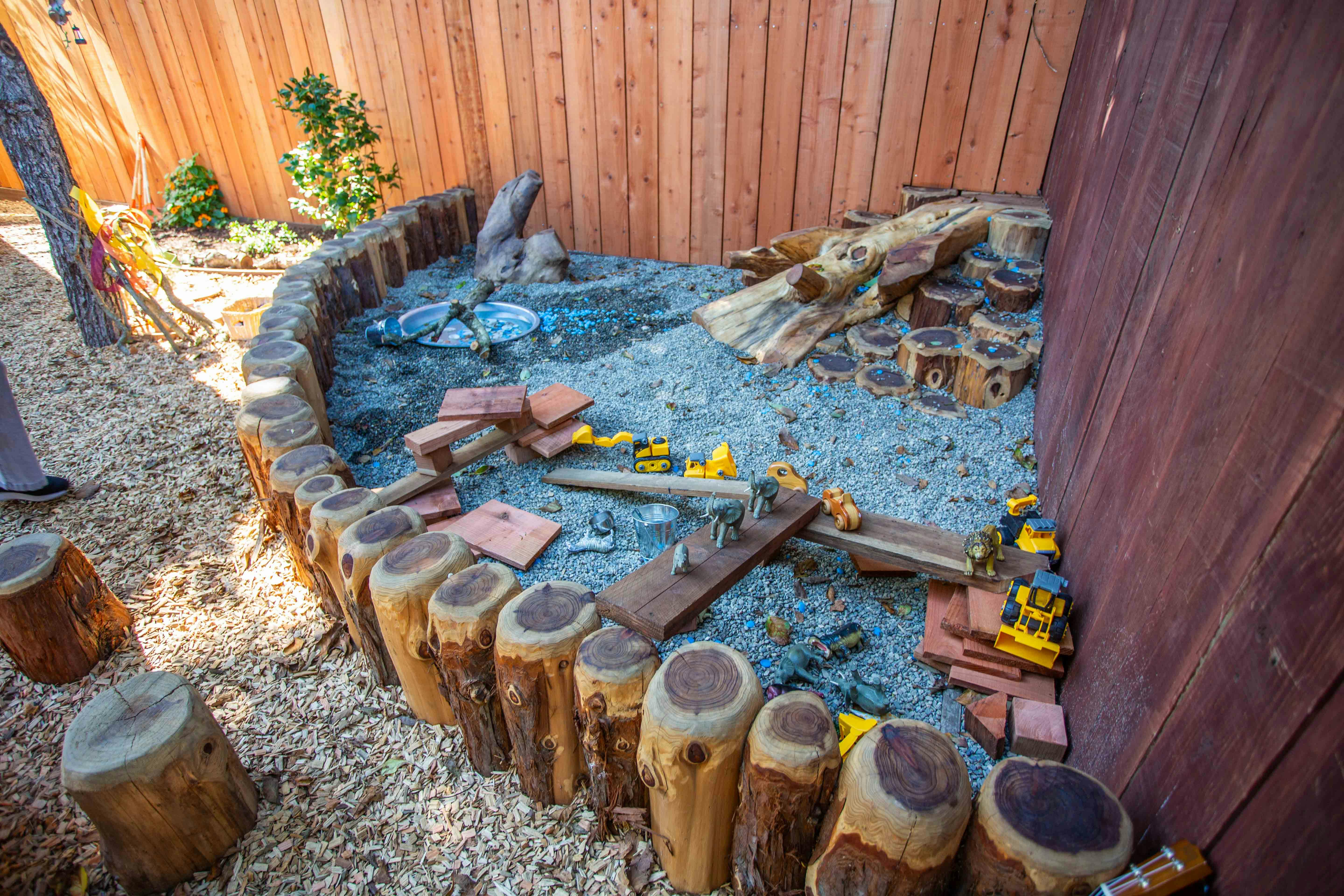 Outdoor play area with sand, wood logs, and toy construction vehicles