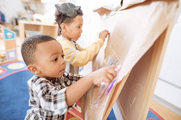 Two children drawing on an easel in a classroom