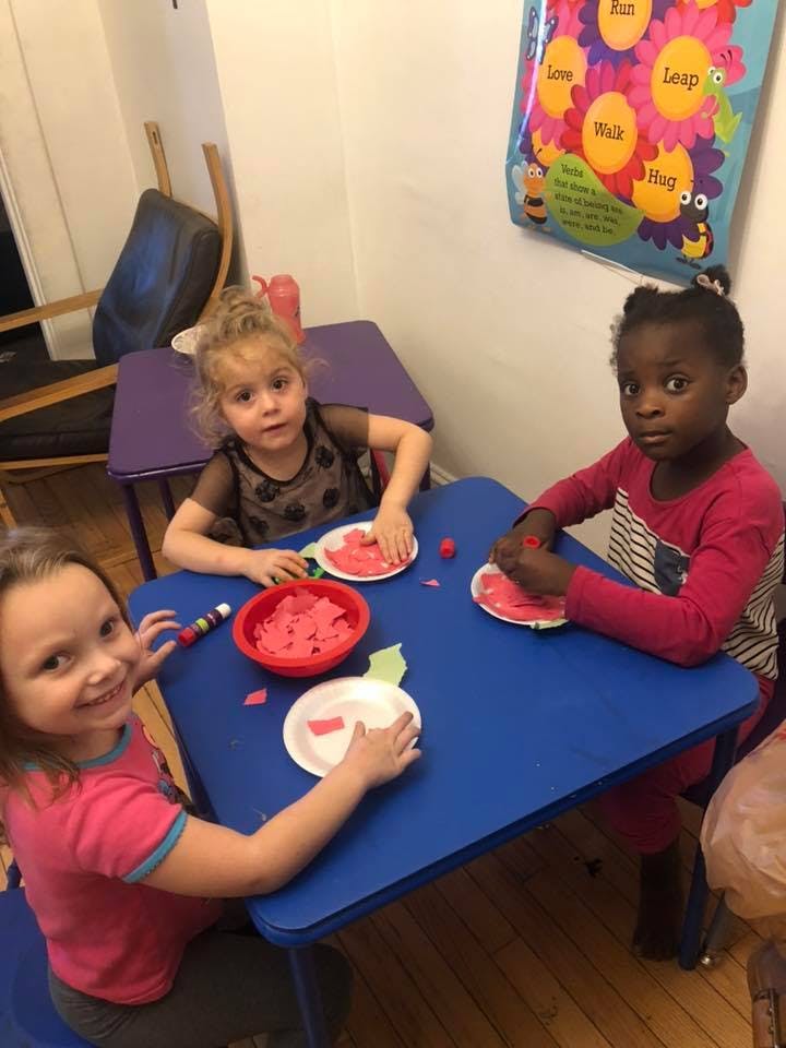 Three children at a table doing an art activity with red paper pieces