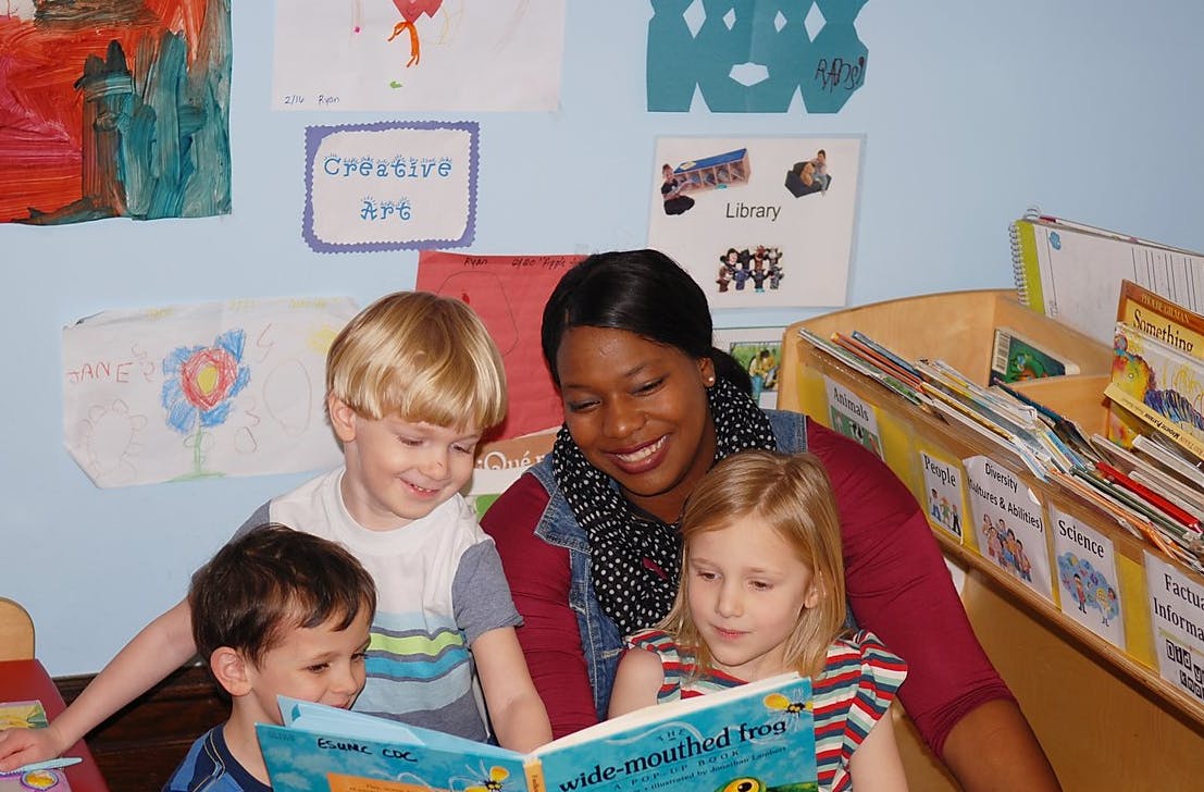Adult and three children reading a book together in a classroom