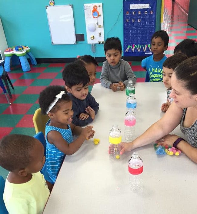 Adult and children at a table with colorful bottles and small objects