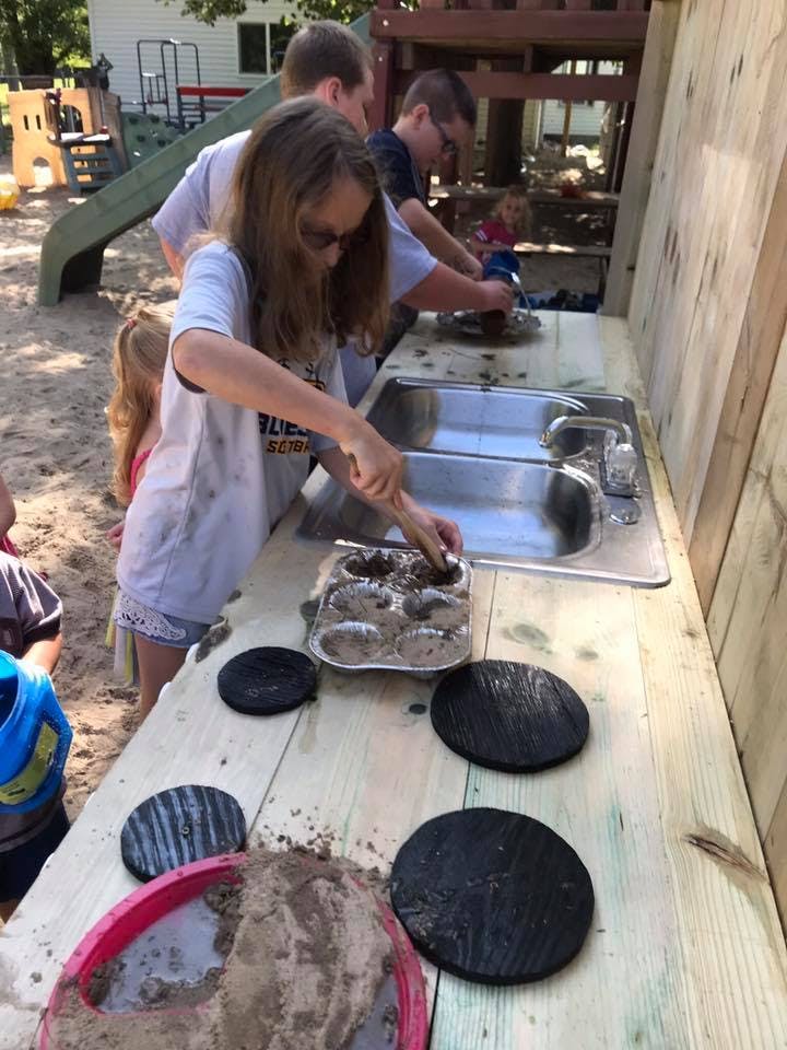 Person playing with mud in a muffin tin at an outdoor sink