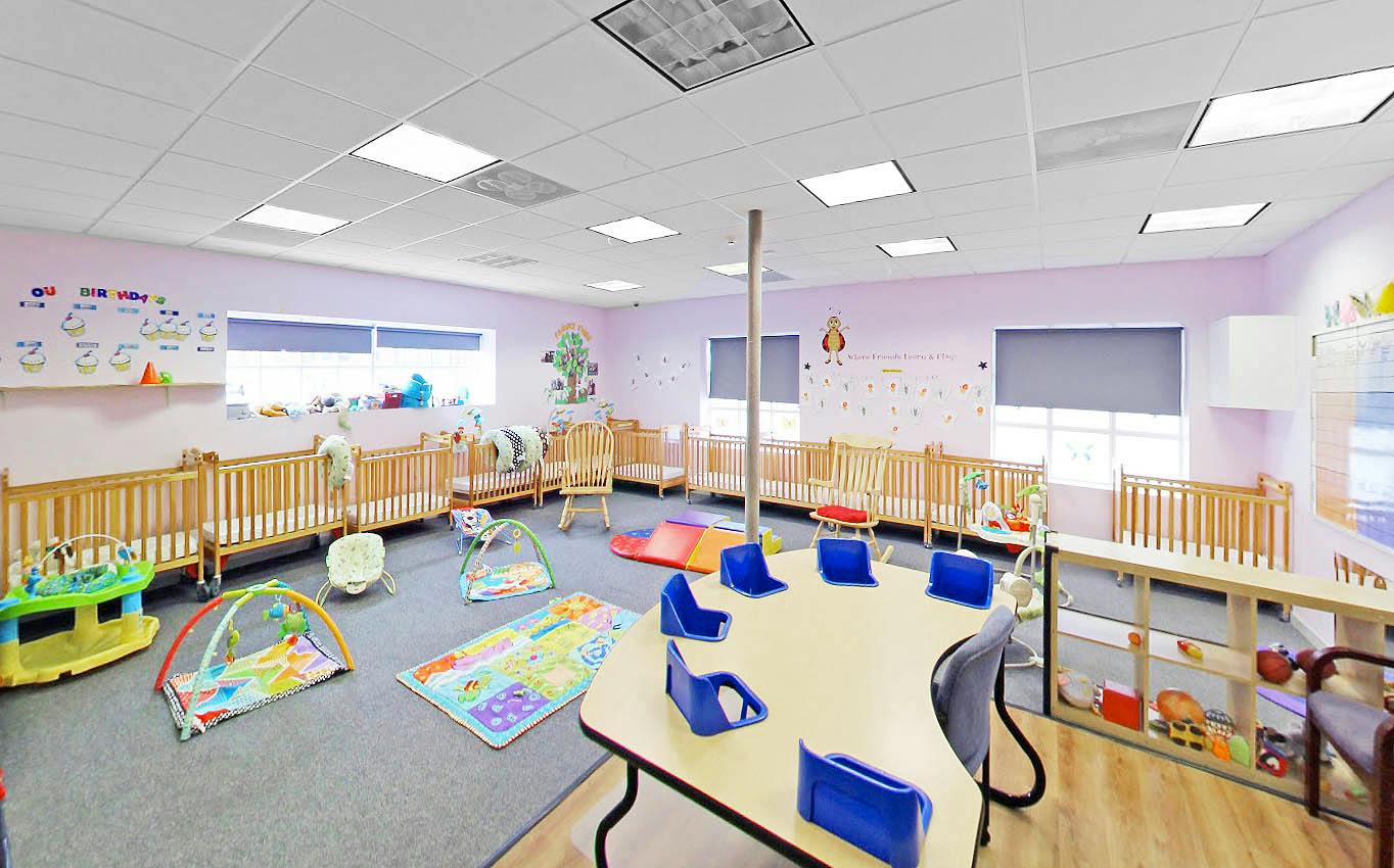 Childcare room with multiple cribs, activity mats, and a table with chairs