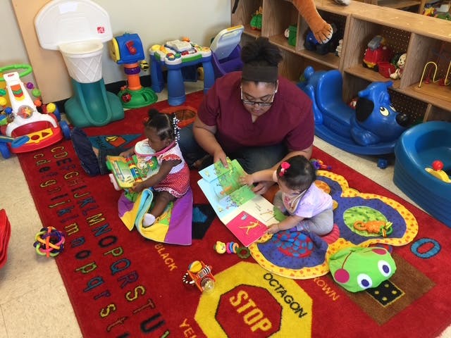 Adult and two children looking at books on a rug in a play area