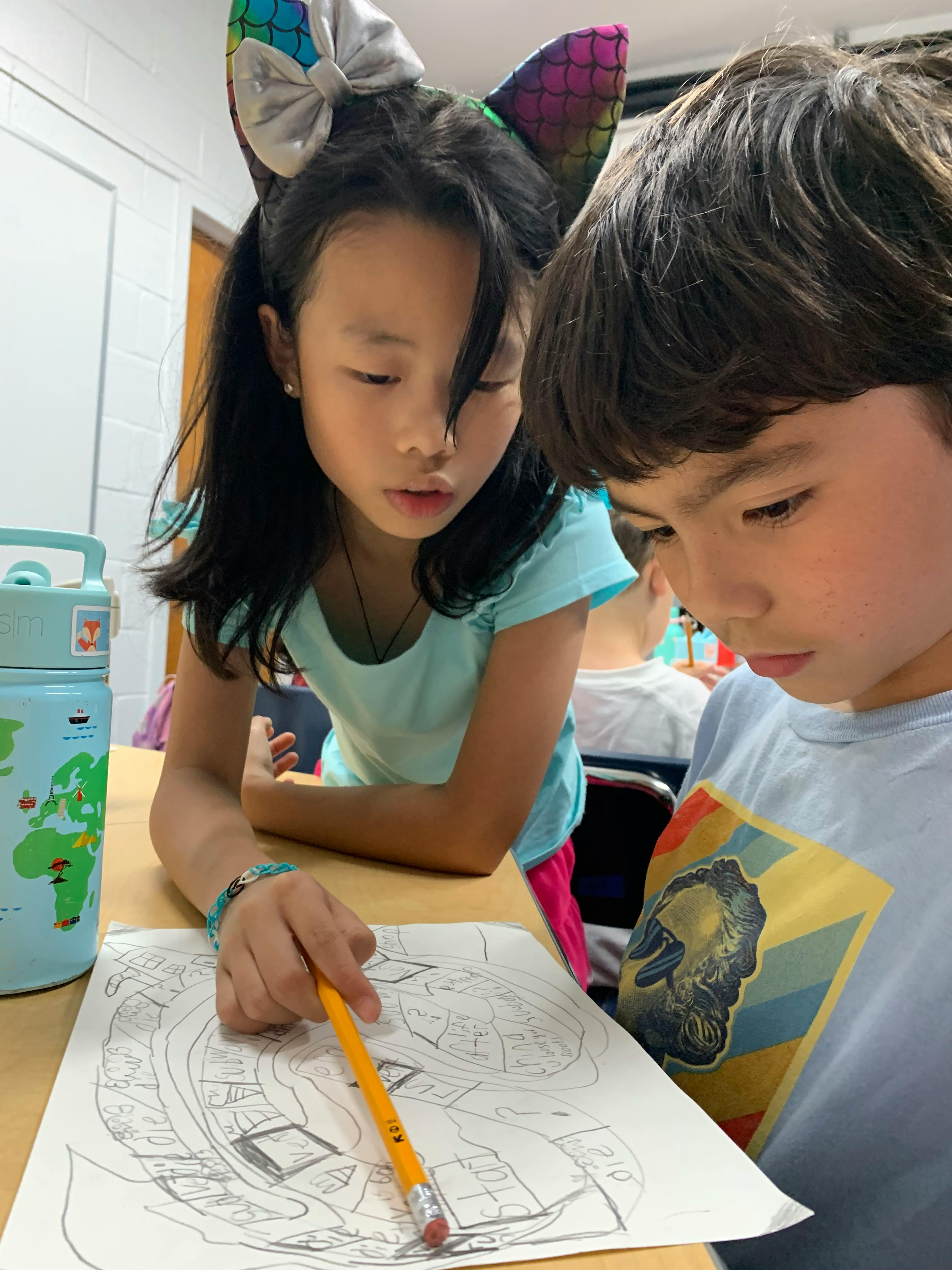 Two children looking at a worksheet with drawings on a desk