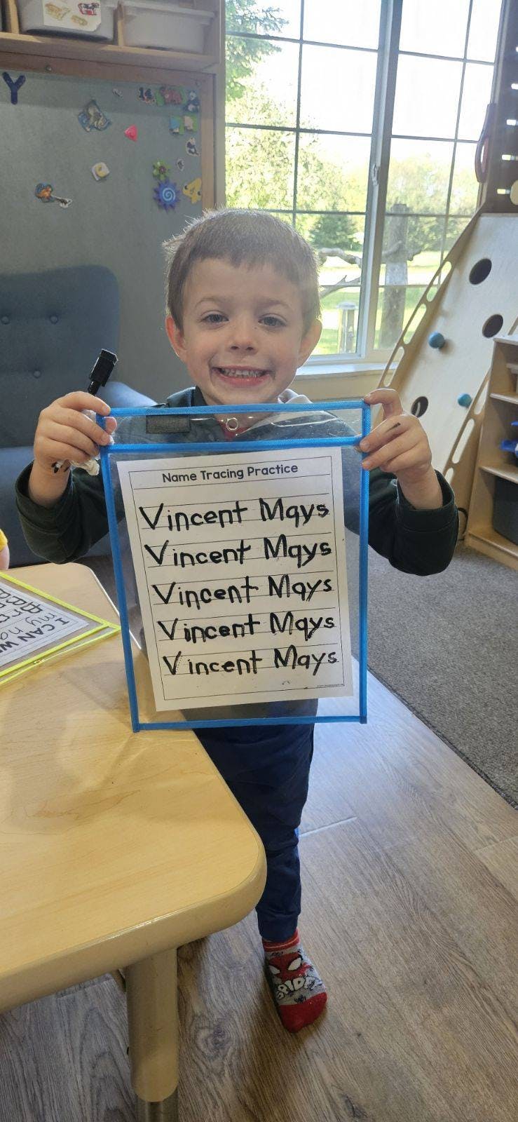 Child holding up a name tracing practice sheet with "Vincent Mays" written on it