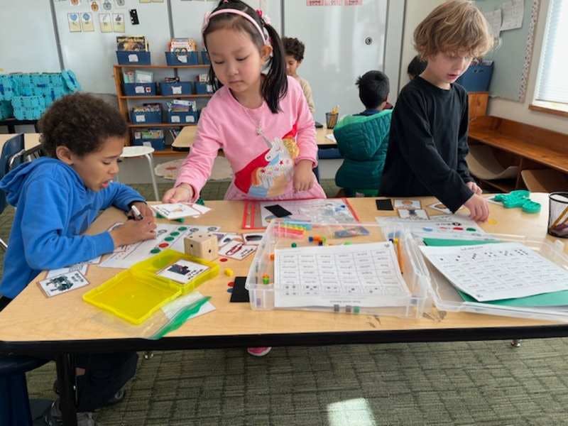 Three children working with learning materials at a table in a classroom