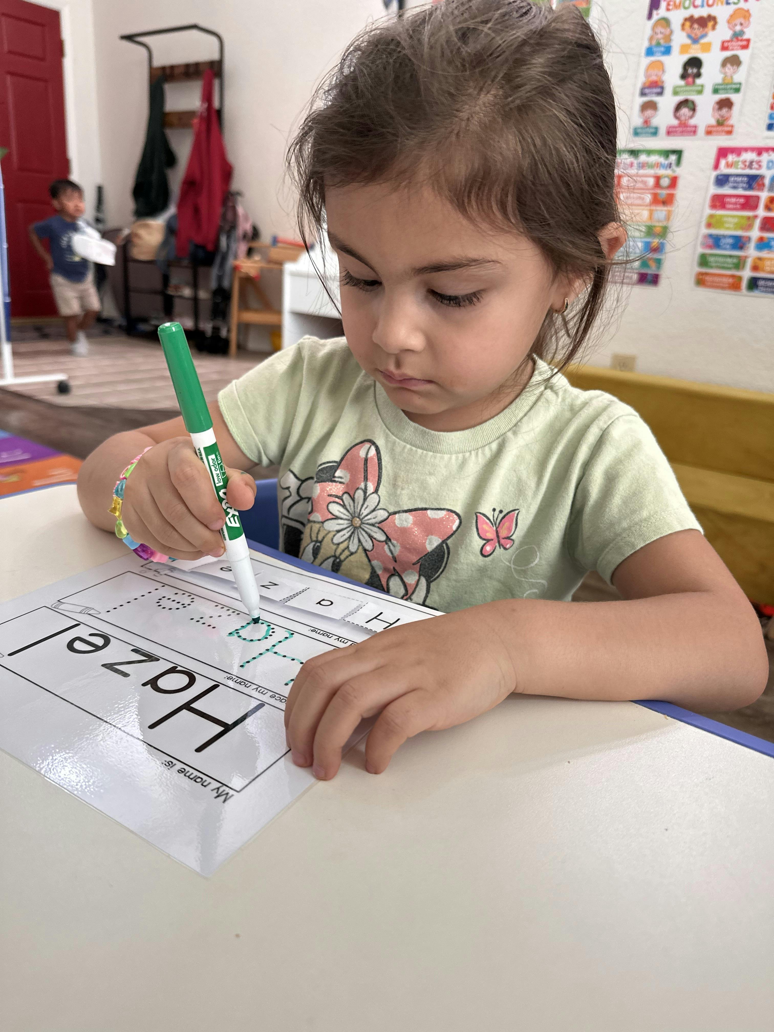 Child practicing writing the name Hazel on a worksheet with a marker