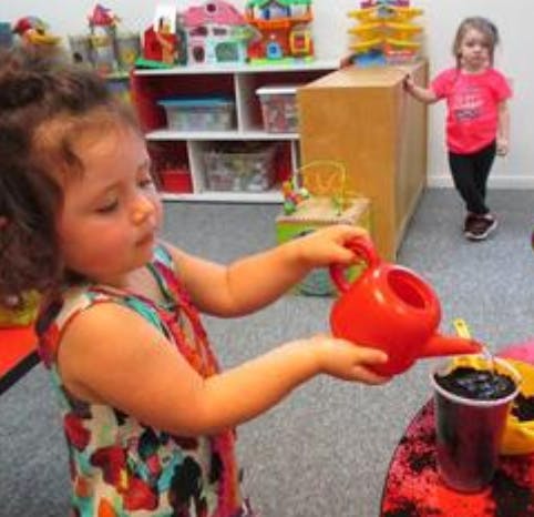 Child pouring water from a watering can into a cup