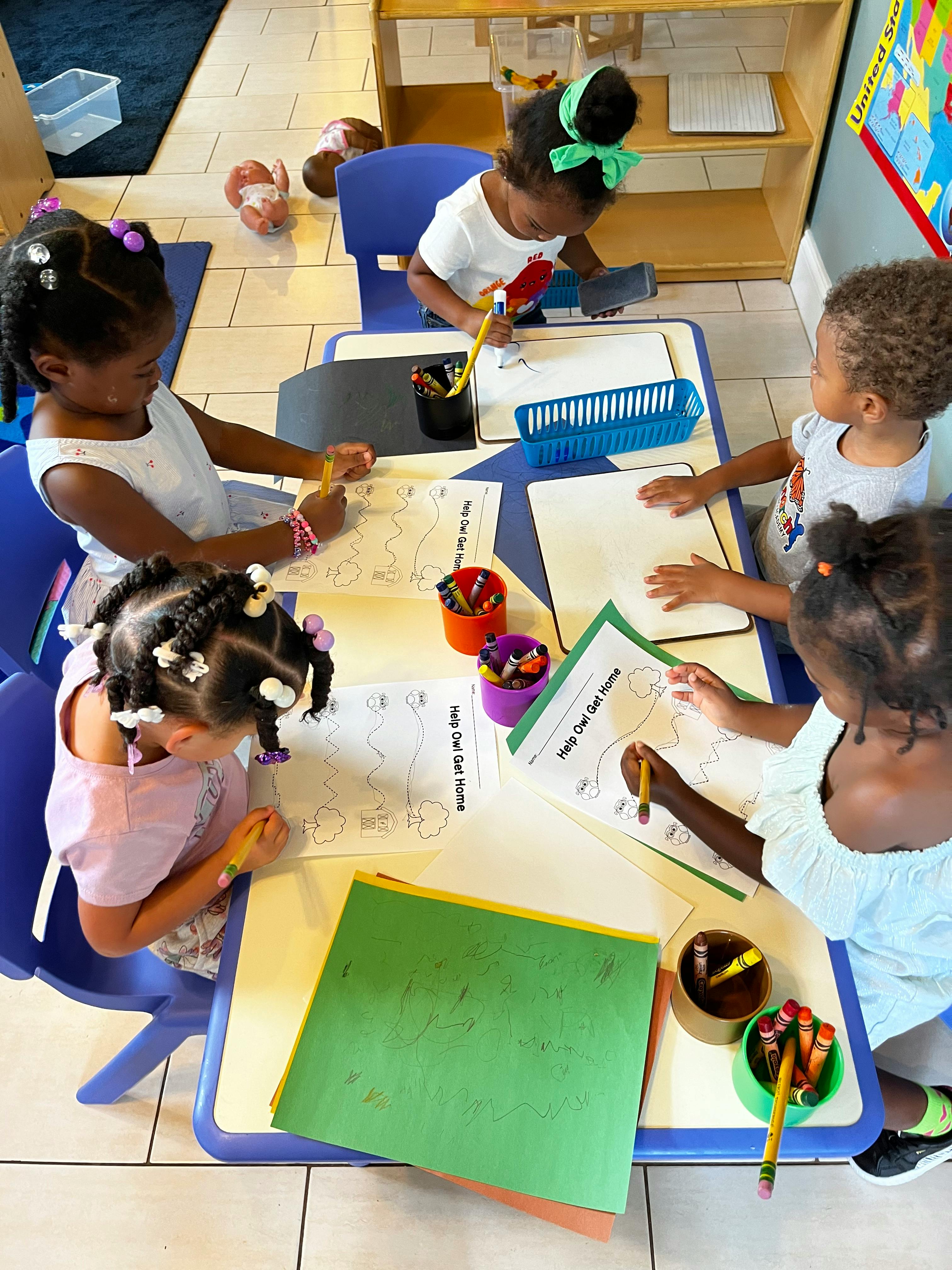 Four children sitting at a table drawing and writing on paper with crayons and paper