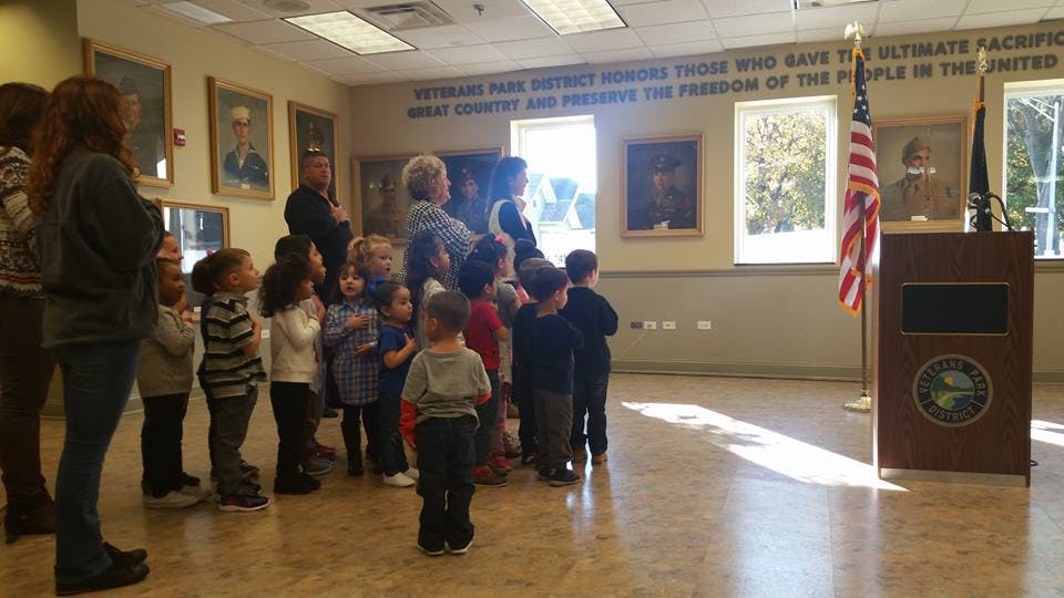 Adults and children standing in a room with a podium and flags