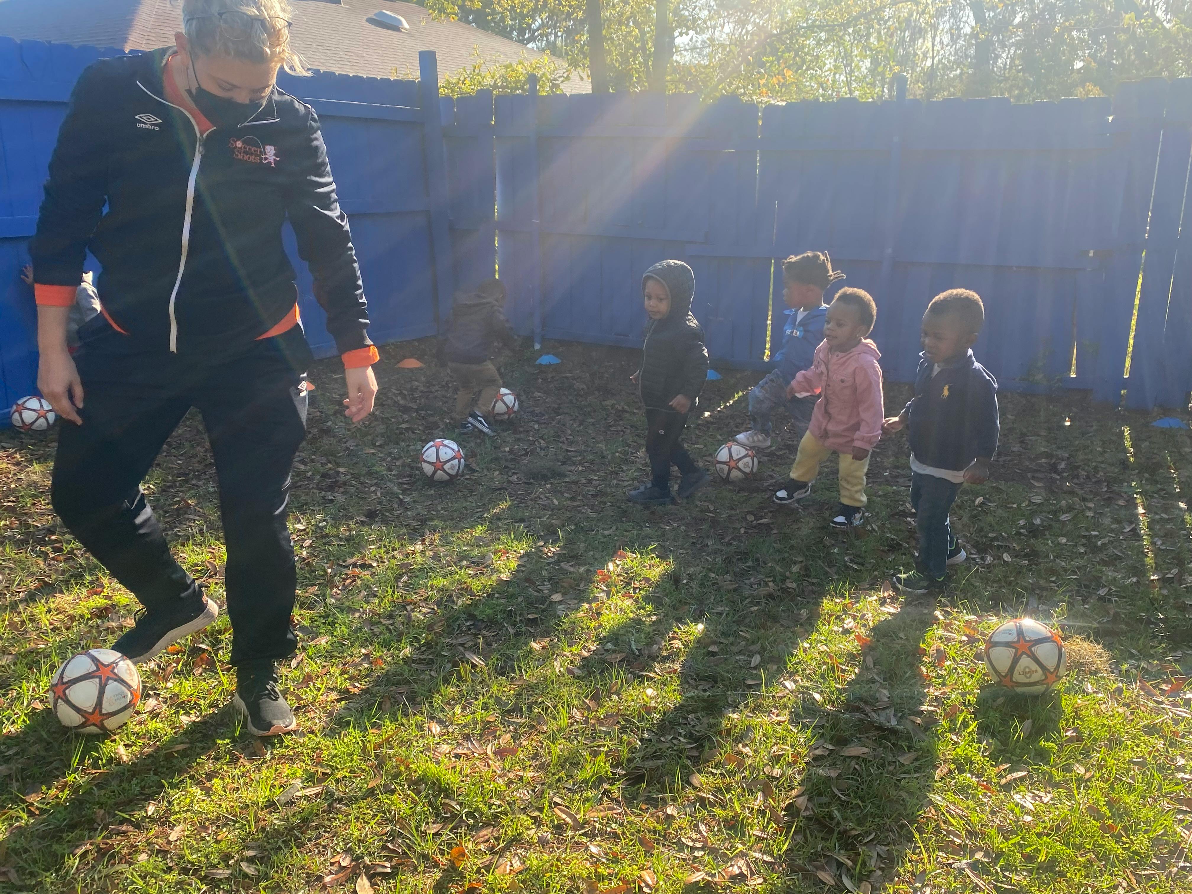 Adult coach and several young children practicing with soccer balls outdoors