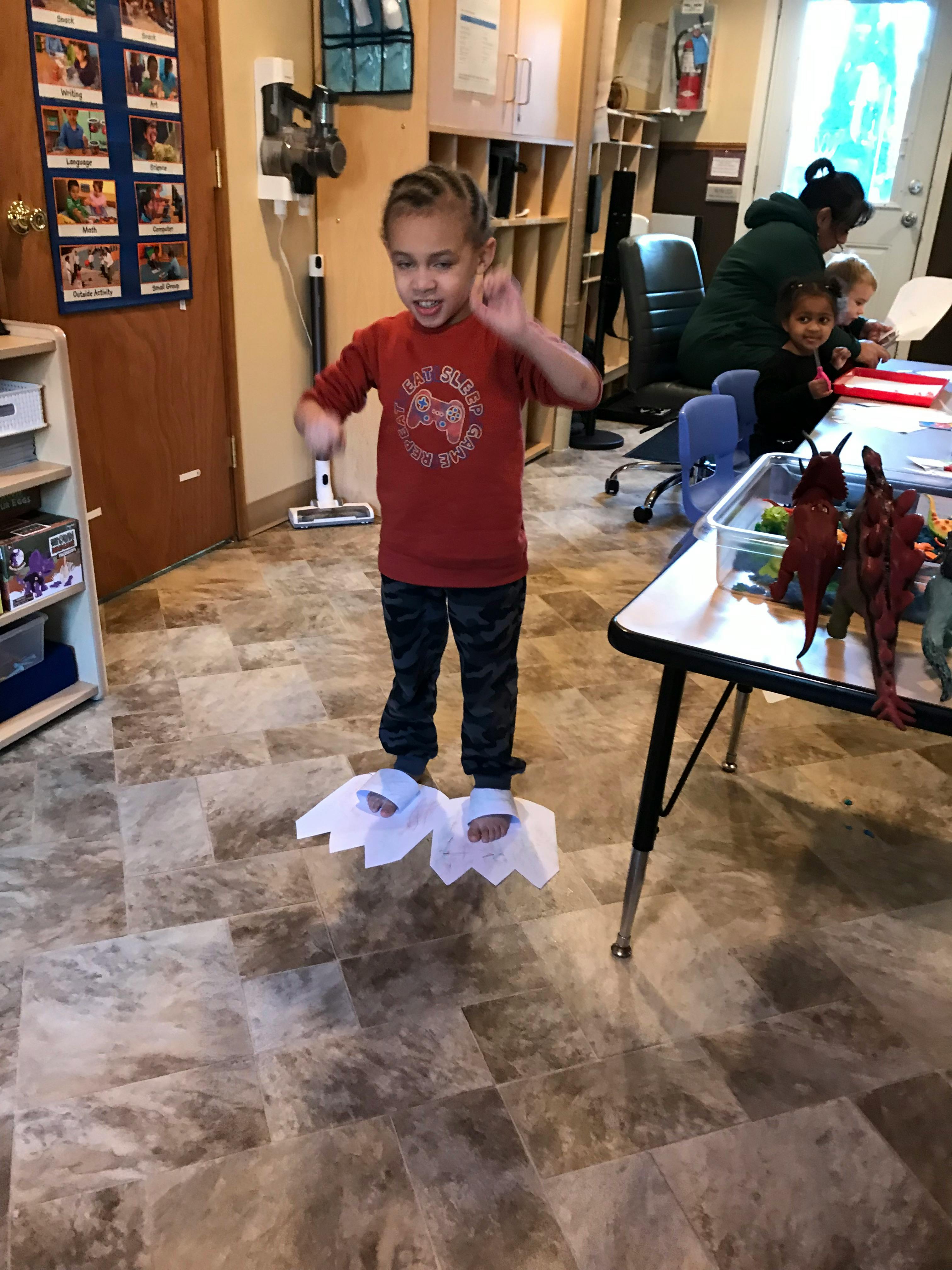 Child standing on paper cutouts in a classroom