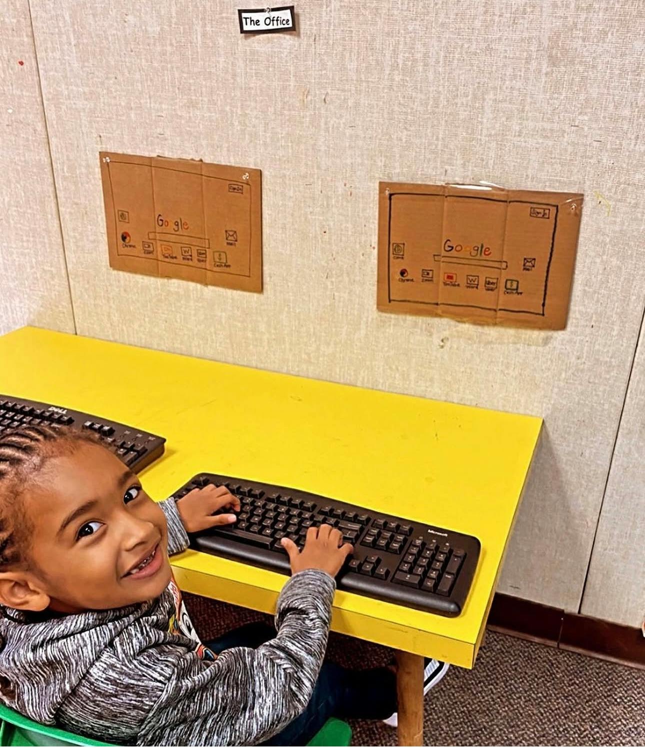 Child typing on a keyboard at a desk with cardboard signs of Google search