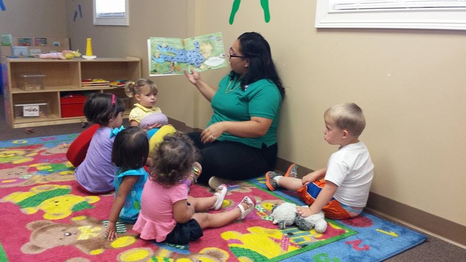 Person reading a book to children sitting on a rug