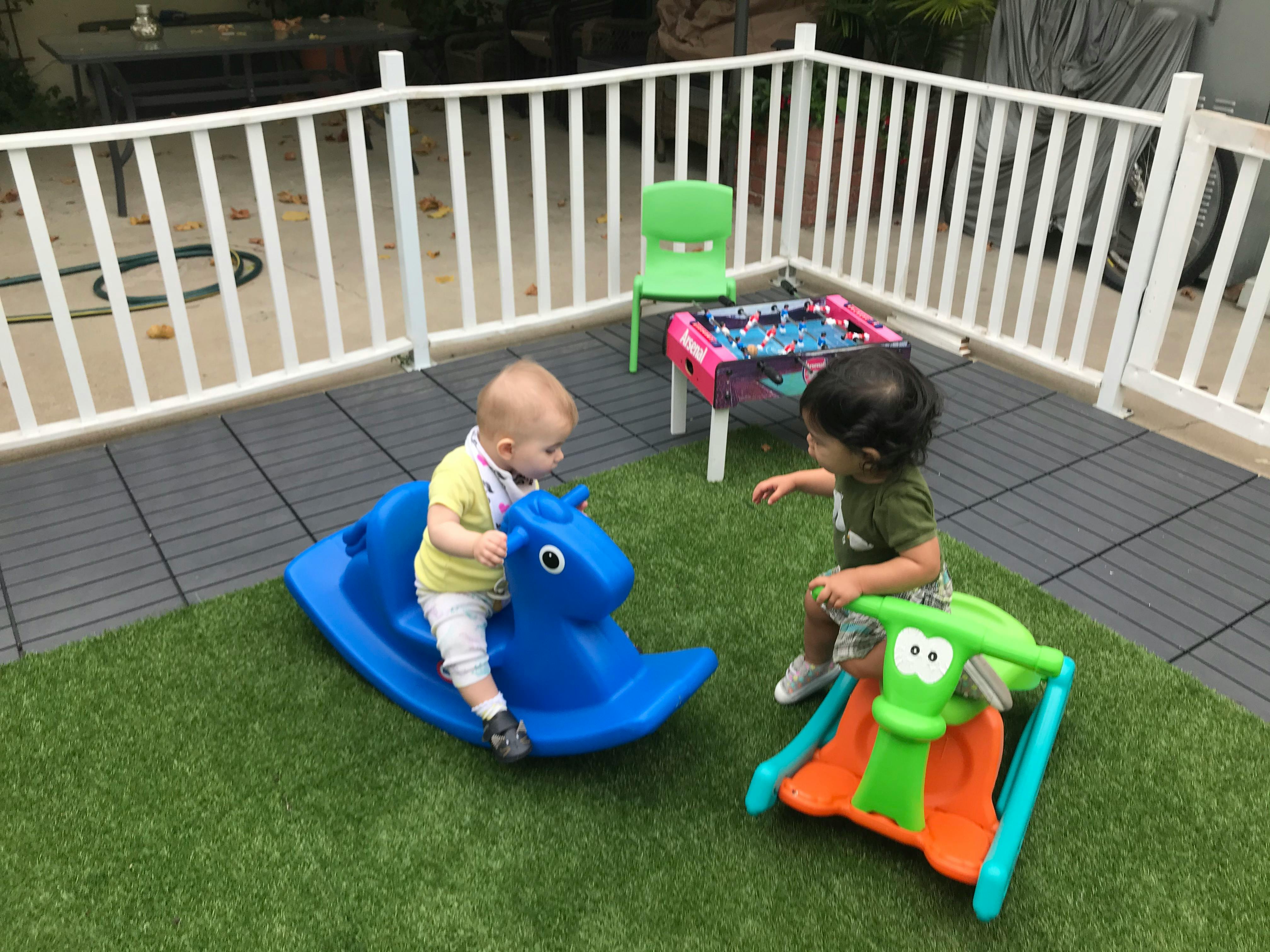 Two children playing with rocking toys on artificial grass