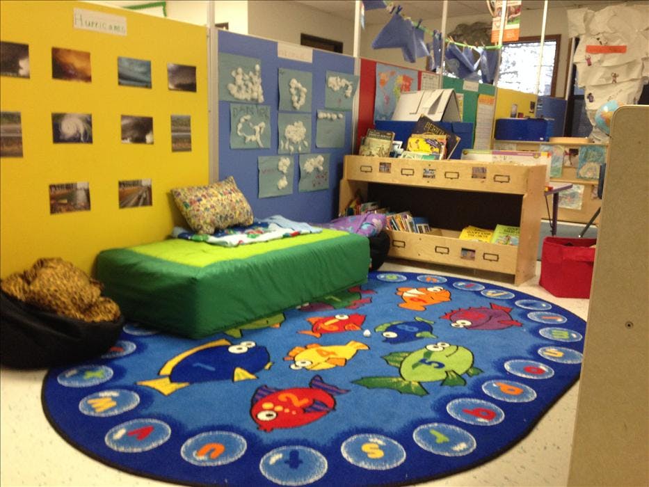 Classroom corner with a reading nook, bookshelf, and fish-themed rug