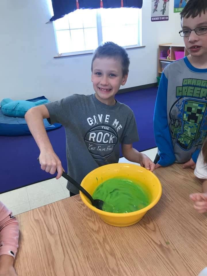 Child stirring green mixture in a yellow bowl