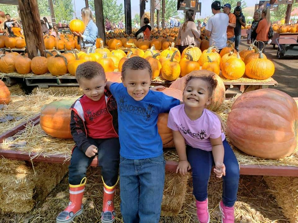 Three children sitting on hay bales with pumpkins