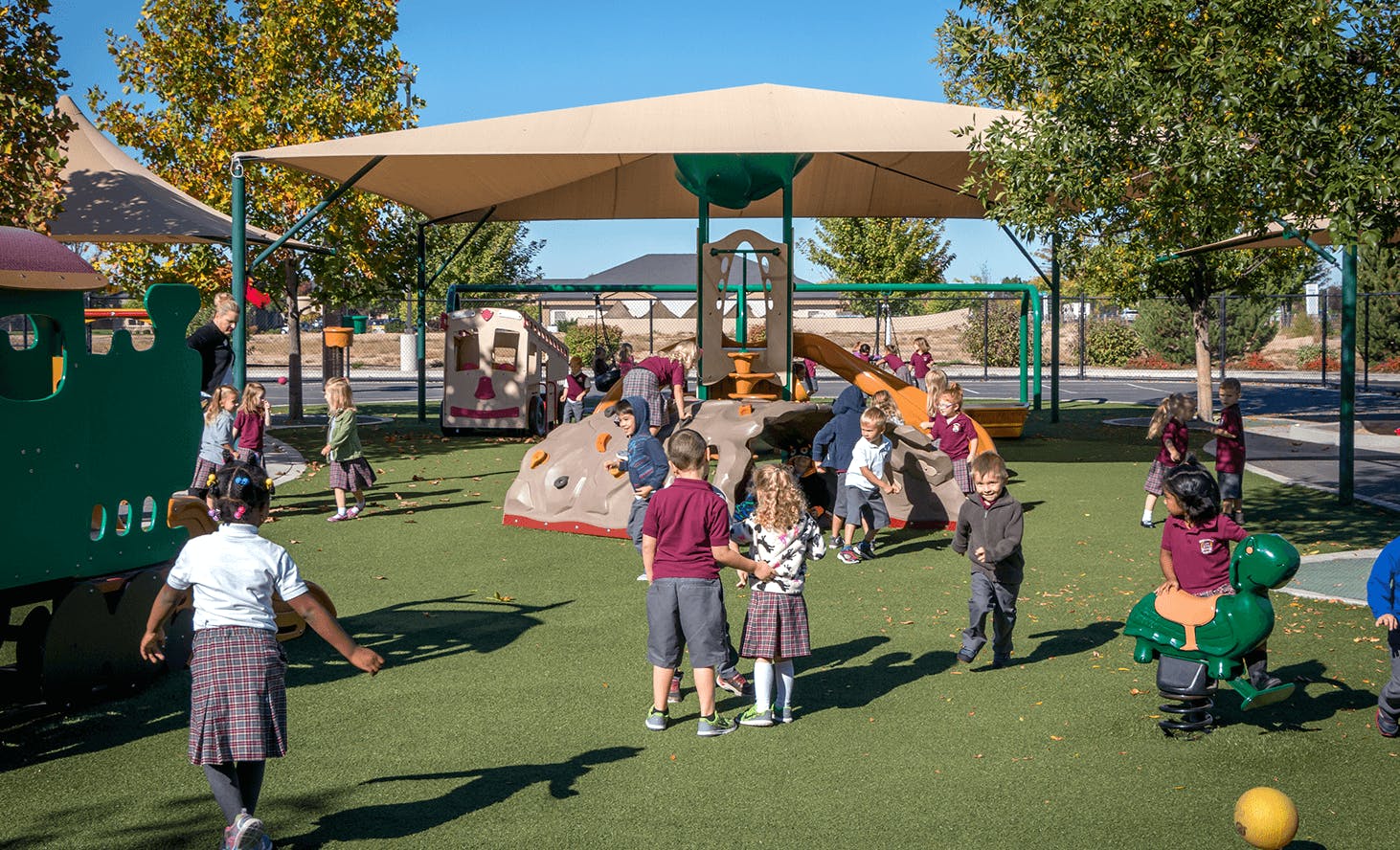 Children playing on a playground with play structures and a shade canopy