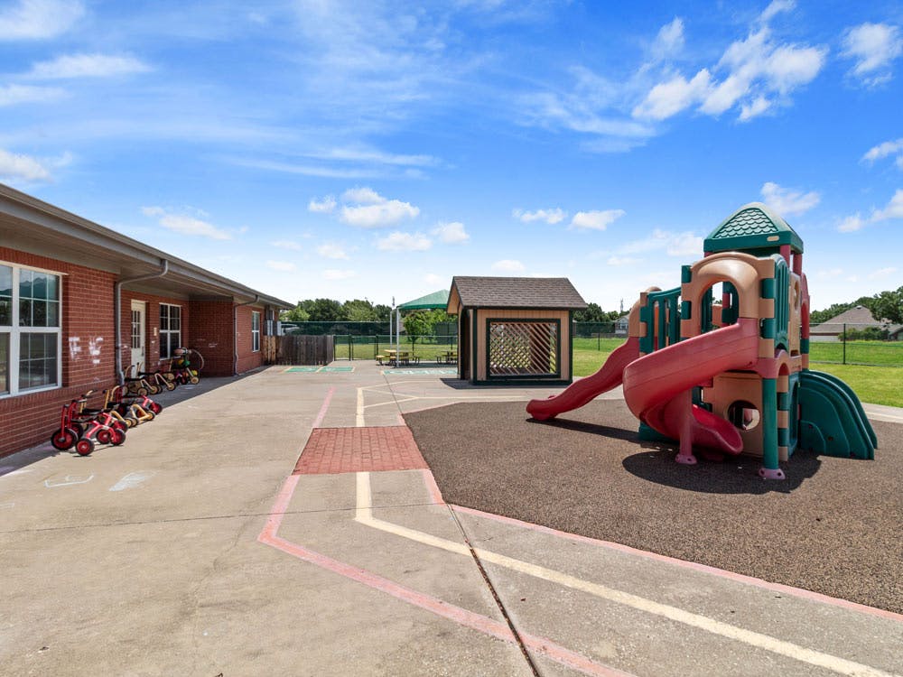 Playground with slides and tricycles in front of a brick building