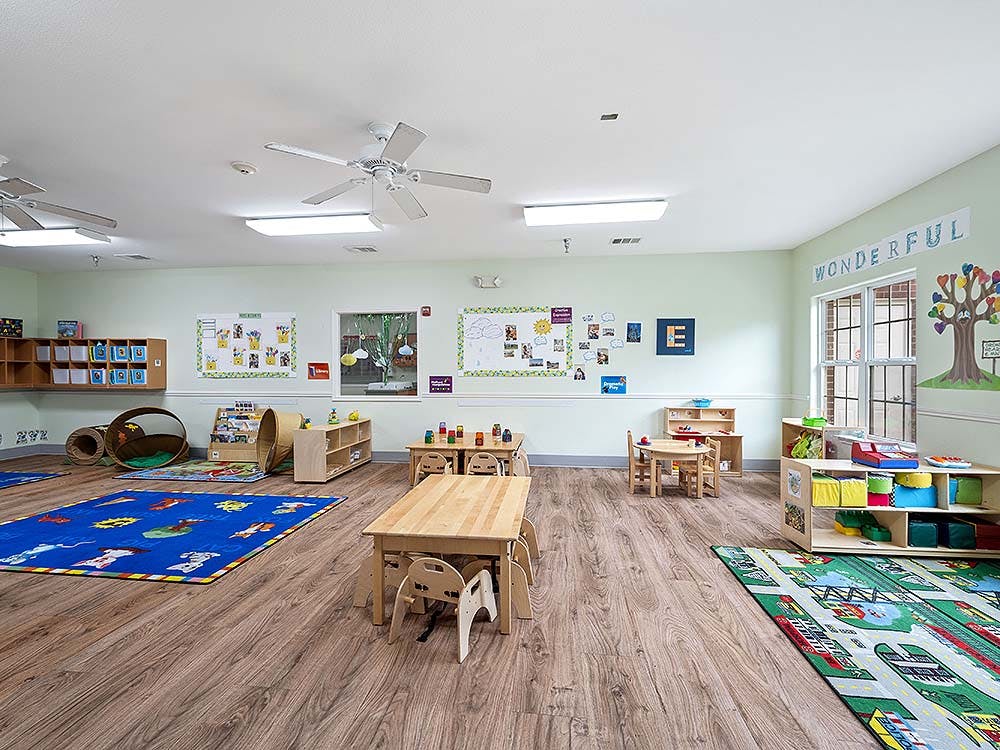 Empty classroom with small tables, chairs, colorful rugs, and play items