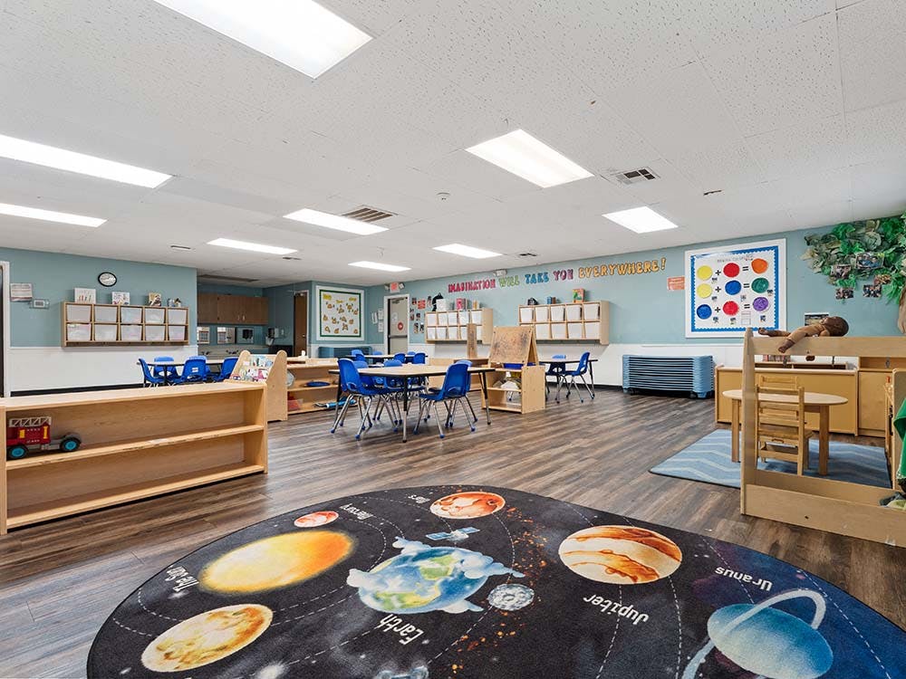 Classroom with tables, shelves, a planet rug, and wall decorations