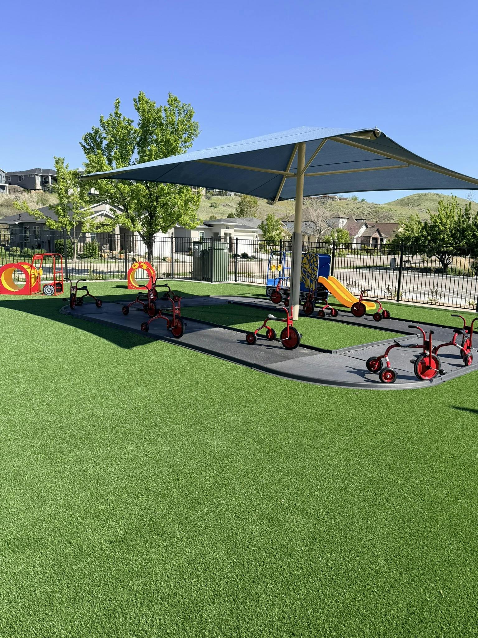 A playground with a blue shade structure over tricycles on a track