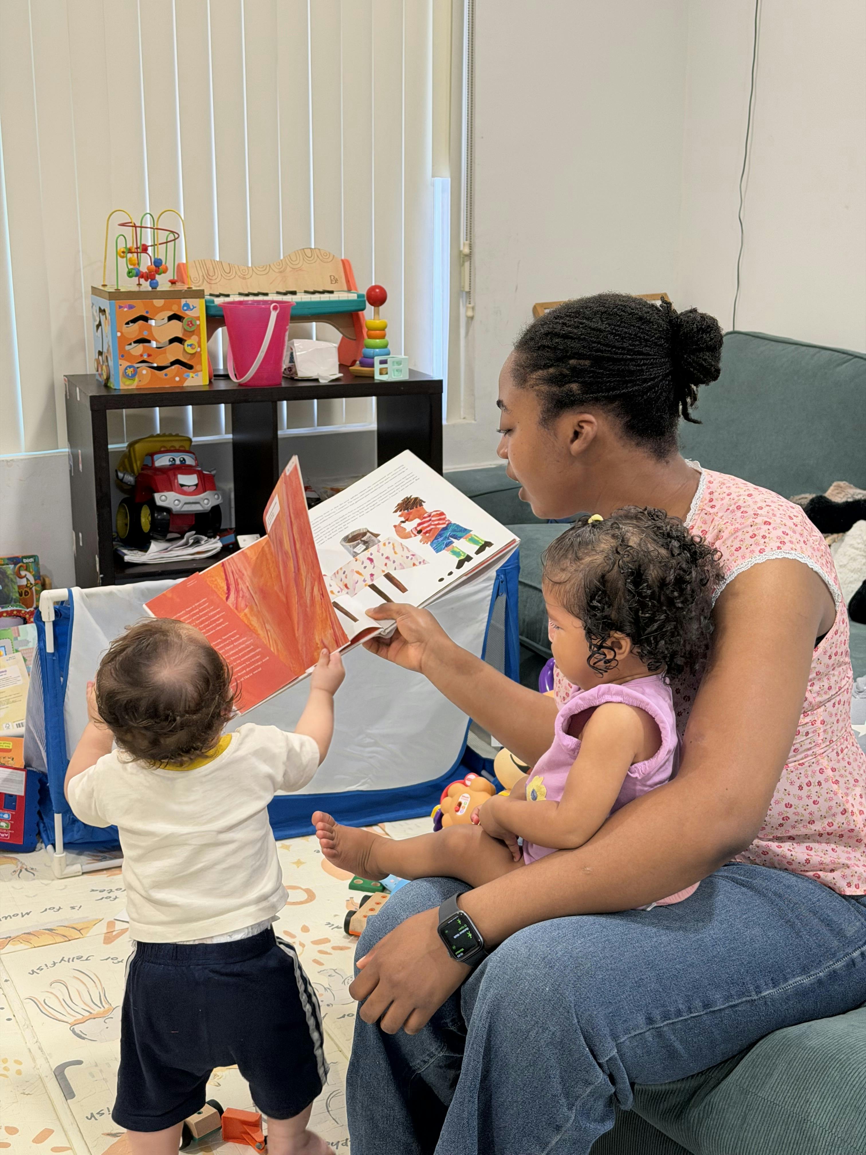 Person reading a book to two children in a playroom